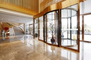 Un hall d’entrée moderne avec une entrée en verre incurvé, un sol en marbre et un escalier menant à un niveau supérieur.