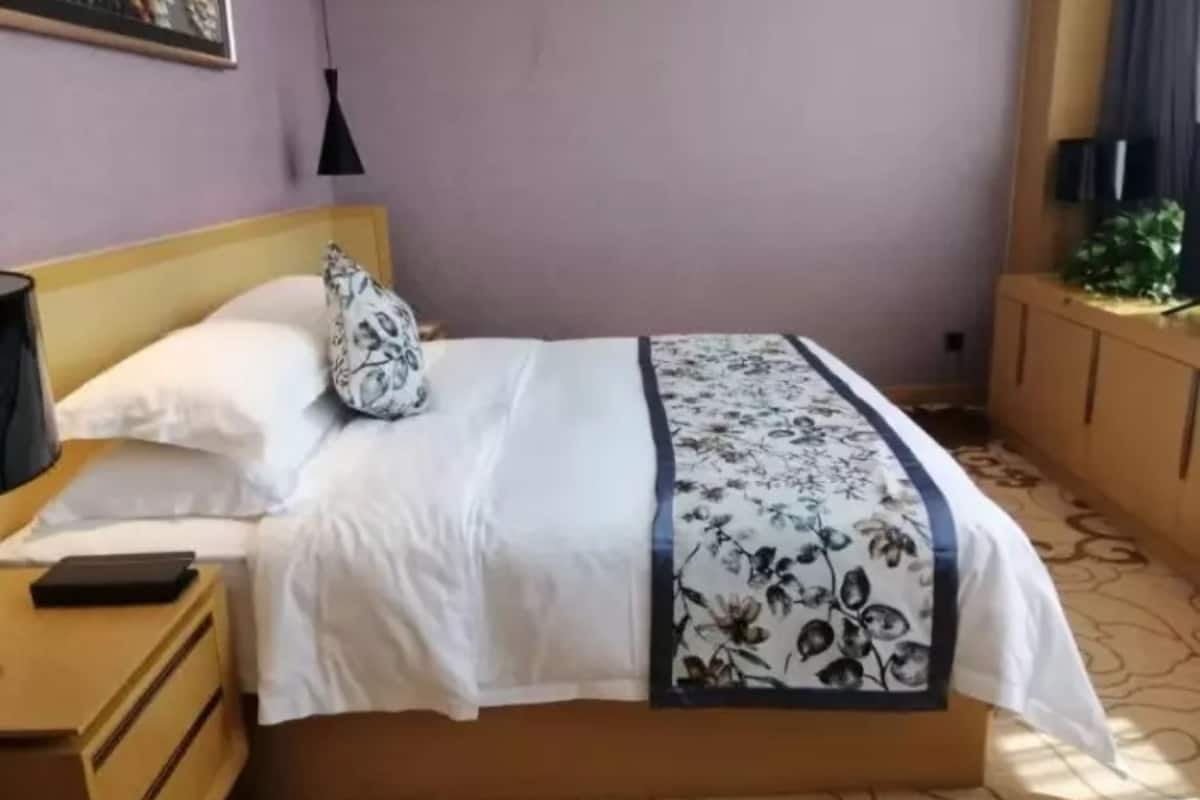 En snyggt bäddad säng med ett blommigt sängöverkast, en sänglampa och ett litet träbord bredvid sängen med en telefon på.