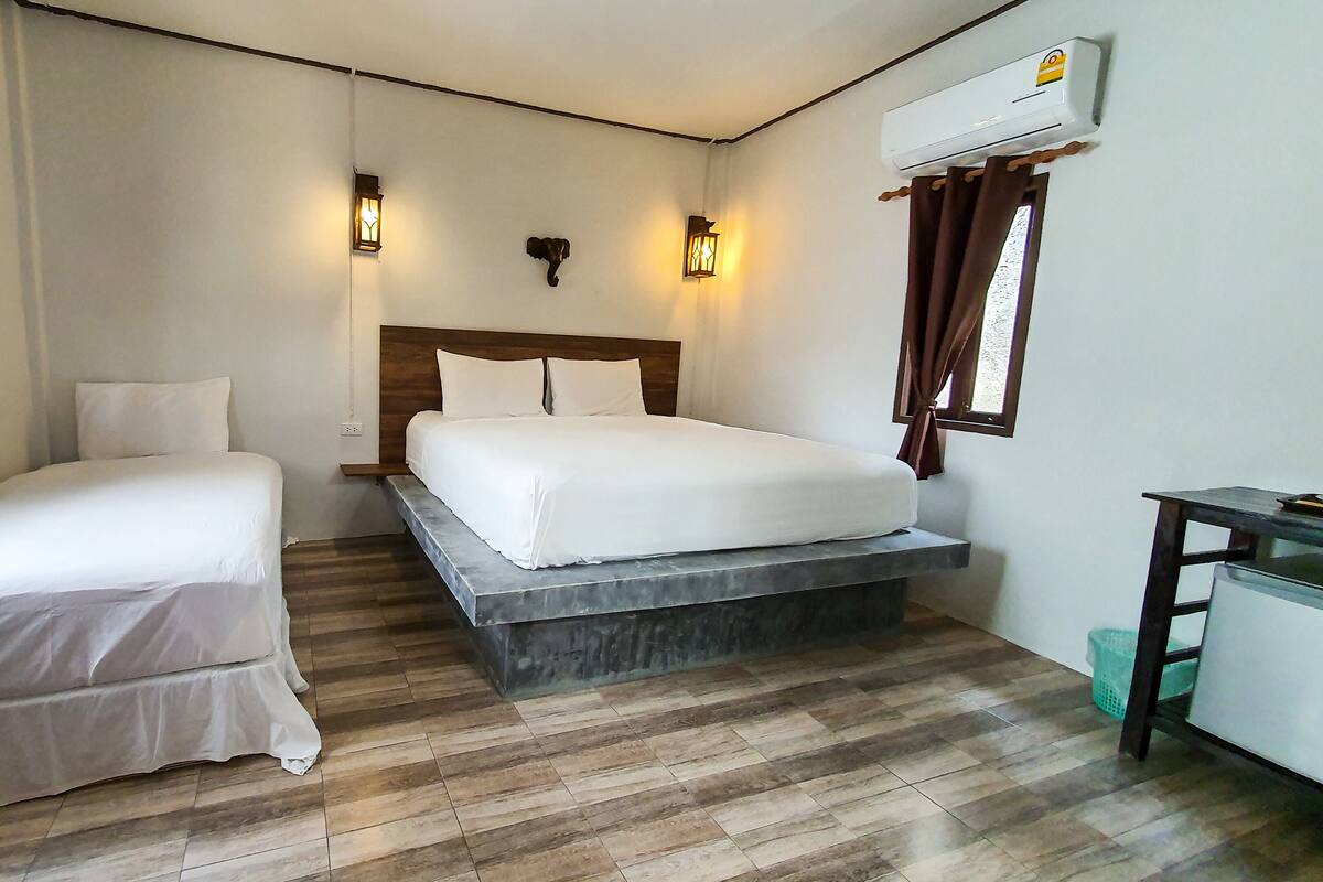 A hotel room with two beds, a wooden floor, an air conditioning unit, and a small desk.