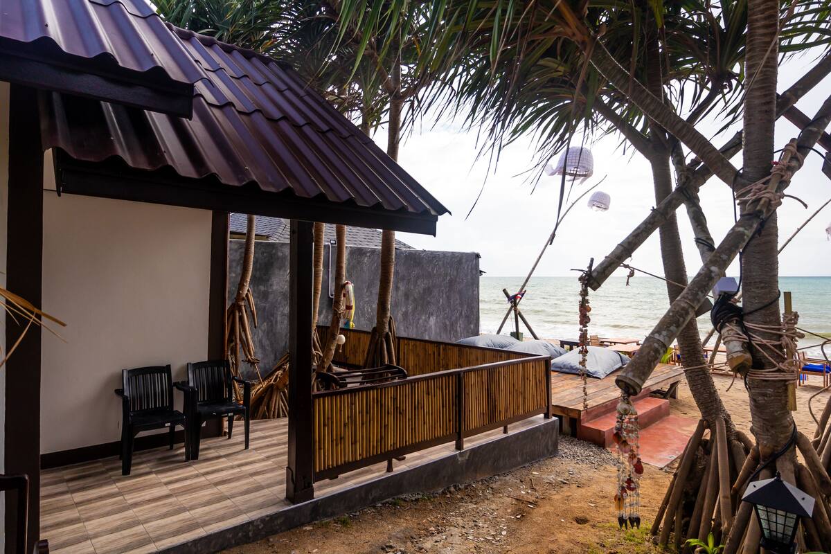 A beachside wooden structure with a corrugated metal roof, two black chairs, and a wooden bench.