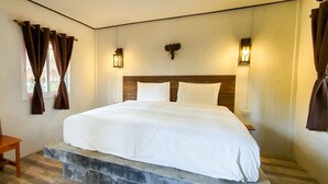 Un dormitorio con cama, cabecera de madera, dos luces fijadas a la pared y una ventana con cortinas.
