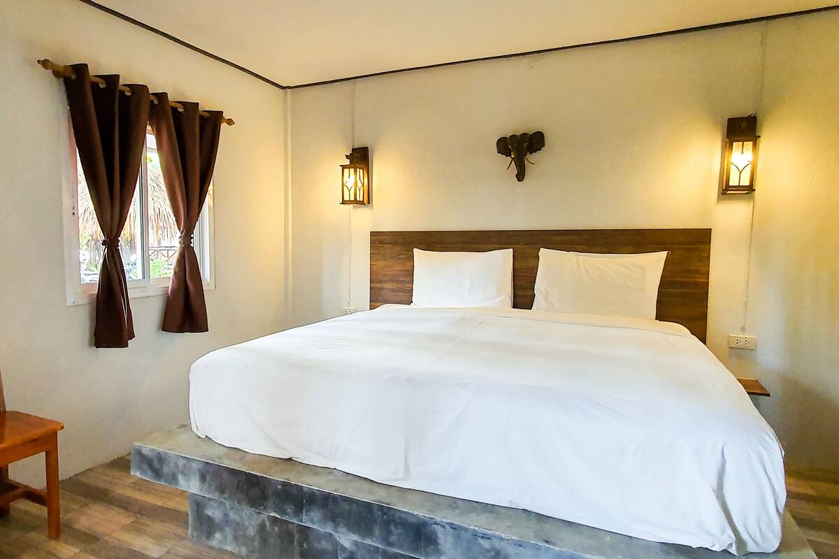 A bedroom with a bed, wooden headboard, two wall-mounted lights, and a window with curtains.