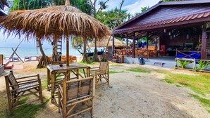 Un restaurante frente a la playa con terraza, techo de paja y vista al océano.