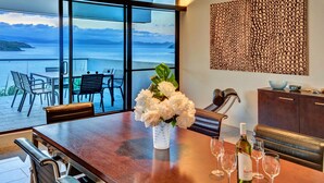 A dining area with a table set for four, a vase of white flowers, and wine glasses. - Waves 3 Luxury 3 Bedroom (Whitsundays)