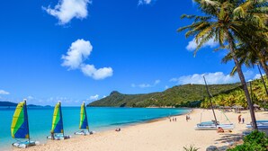 A beach with clear turquoise water, palm trees, and sailboats. - Waves 3 Luxury 3 Bedroom (Whitsundays)