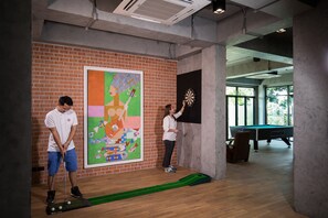 A room with a brick wall, a dartboard, a pool table, and a colorful abstract painting. - S Loft Sport and Wellbeing Hotel (Chiang Mai)