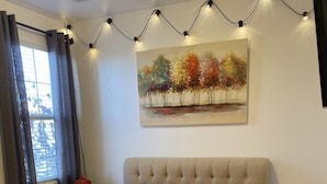 Un dormitorio con cama, mesita de noche, un cuadro y luces decorativas.