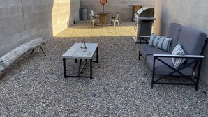 Un patio con una parrilla, asientos y una mesa.