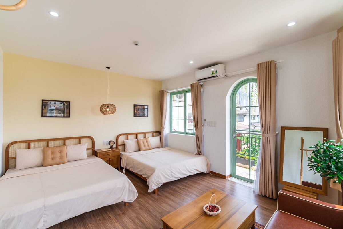 A hotel room with two beds, a wooden table, a mirror, and a window with curtains.