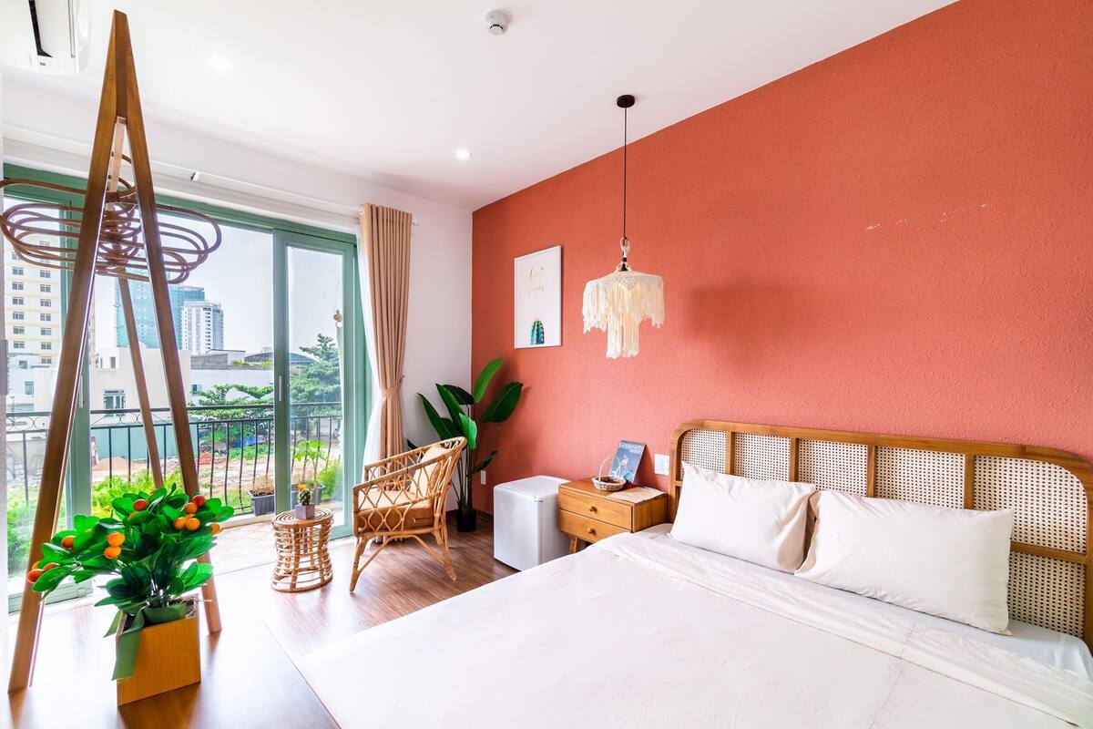 A modern hotel room with a large bed, a wooden ladder, a wicker chair, a small table, and a potted plant.
