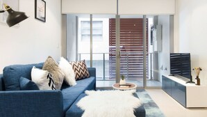 Een moderne woonkamer met een blauwe bank, een zacht wit tapijt en een televisie op een witte kast.