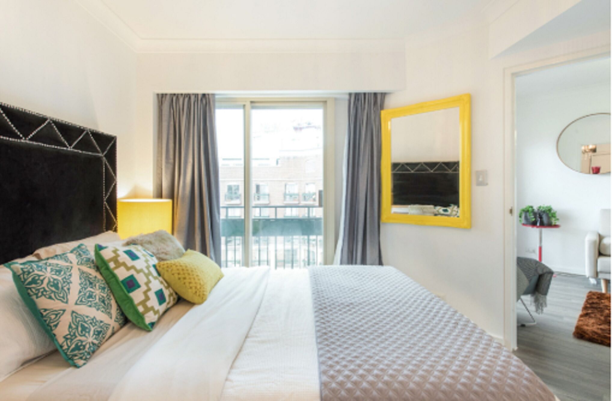A hotel room with a bed, a large window, a mirror, and a balcony.