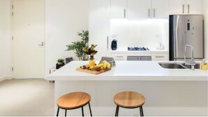 Een moderne keuken met witte kasten, een roestvrijstalen koelkast, een centraal eiland met krukken en een kleine potplant.