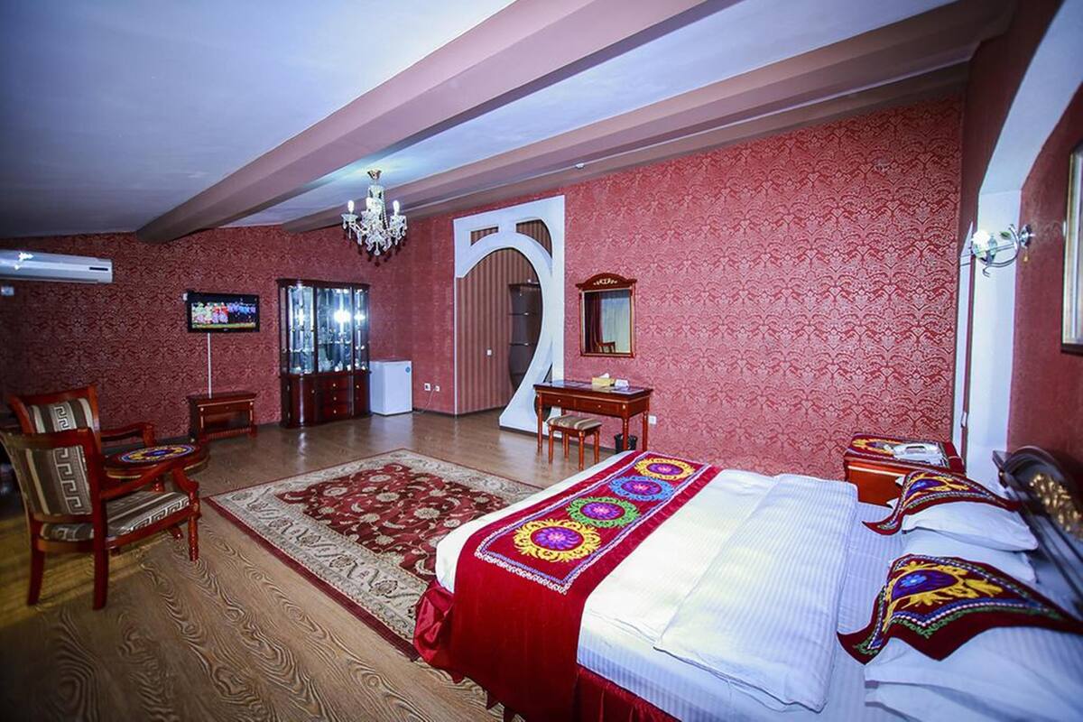 A hotel room with a large bed, a sitting area with a chair and a small table, a television, and a chandelier.