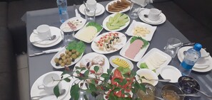 Une table dressée avec divers plats, notamment des fruits, des pâtisseries et une bouteille d’eau.