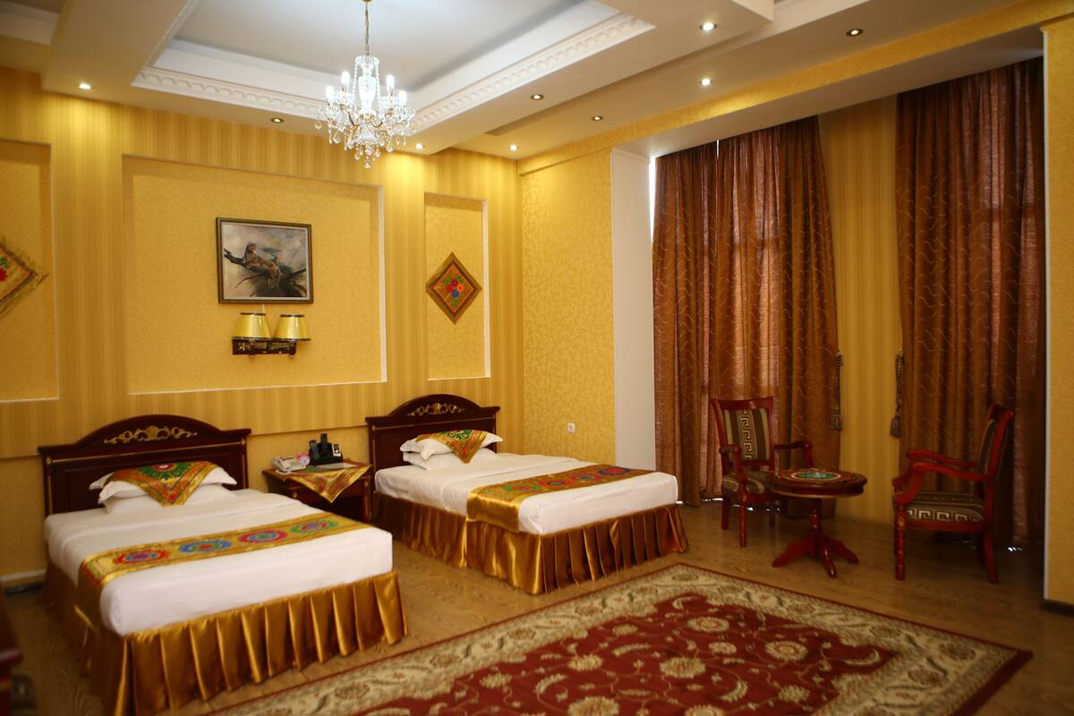 A hotel room with two beds, a chandelier, a red carpet, and a view of the outside.