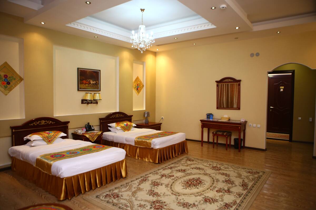 A hotel room with two beds, a desk, a chair, a chandelier, and a large rug.