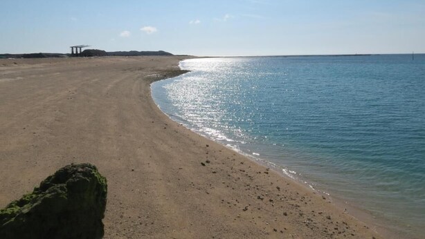 A beach with a rocky outcrop and a structure in the distance. - Hong Hu Ju Captain Sung's House (Baisha)