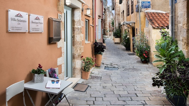 A narrow cobblestone street with a table and chairs set up outside a building, signs indicating 'Villa Splanzia' and 'Boutique Home', and potted plants along the path. - Boutique Home-Splantzia-Roof Garden-2min Harbor (Chania)