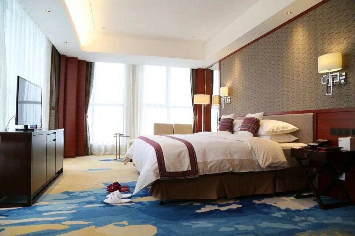 A hotel room with a large bed, a desk, a TV, and a window with curtains.
