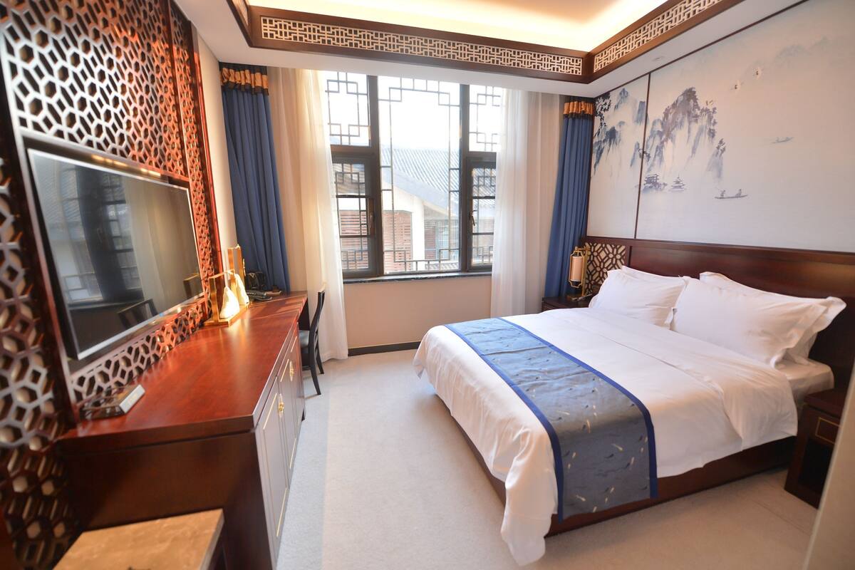 A hotel room with a large bed, a TV on a wooden desk, and a window with curtains.