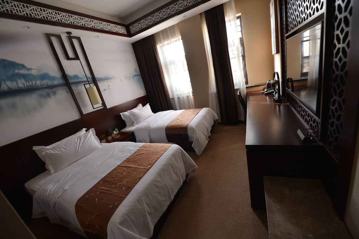 A hotel room with two beds, a desk, a mirror, and a painting on the wall.