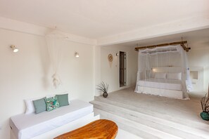 Ein Schlafzimmer mit einem weißen Bett, einer Holzbank, einem weißen Sofa mit grünen Kissen und einer Treppe, die auf einen Balkon mit weißem Baldachin führt.