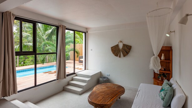 Una habitación moderna con un ventanal grande, un banco de madera, un sofá blanco y una pequeña escalera que lleva a un espacio exterior.
