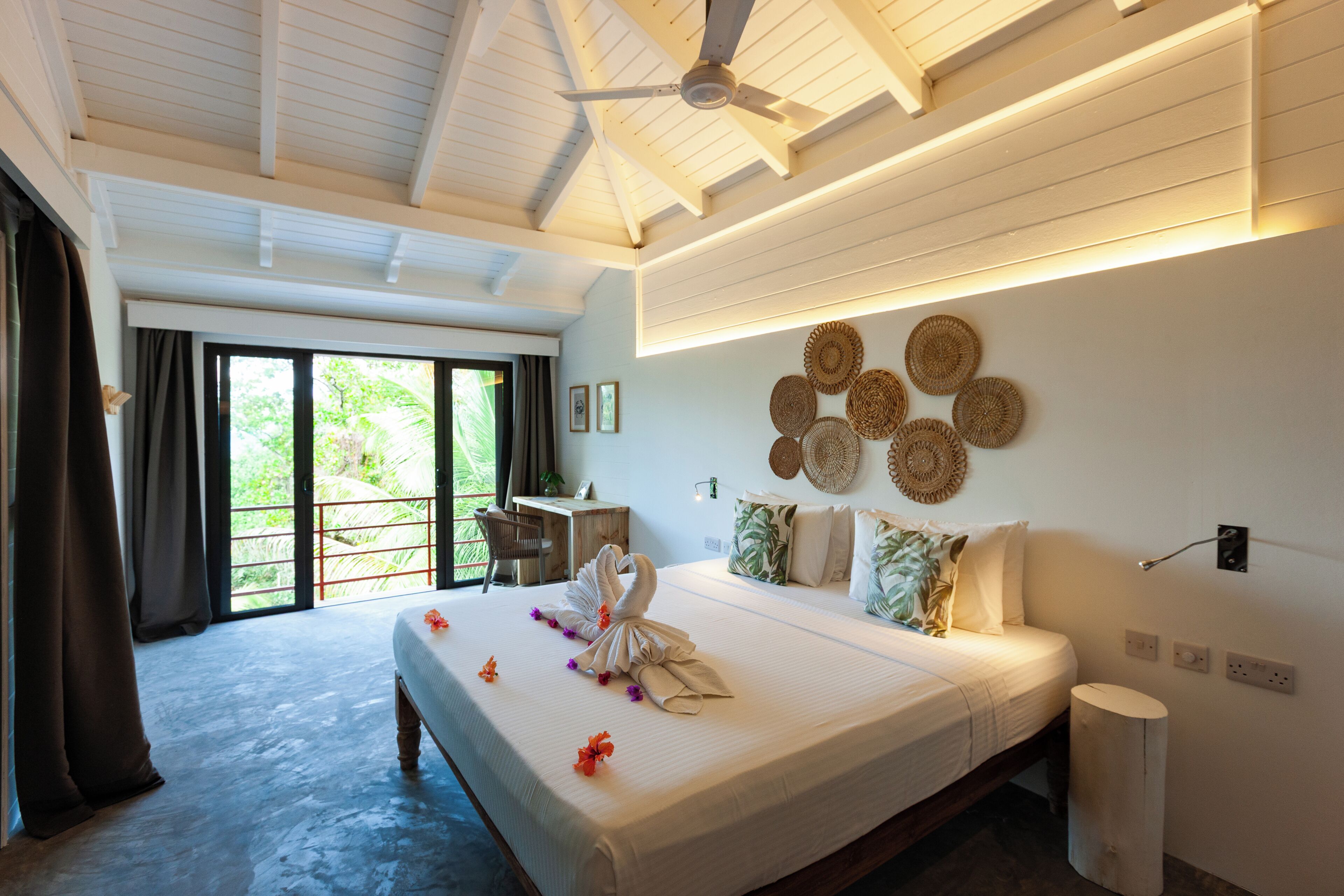 A hotel room with a large bed, a desk, and a view of greenery outside.