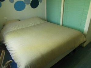 Un lit simple avec un matelas et des oreillers blancs, un mur orné de motifs circulaires et une fenêtre avec des stores.