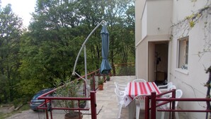 Une terrasse avec une table et des chaises, entourée de plantes en pot et d’une rambarde rouge.