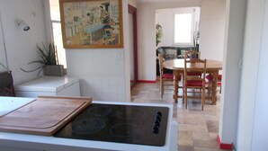 Une cuisine équipée d’une cuisinière, d’une table à manger et de chaises. Un tableau est accroché au mur et une plante est posée sur le comptoir.