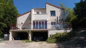 Un immeuble de deux étages avec un garage, un balcon doté d’une rambarde rouge et une plante en pot sur le balcon.