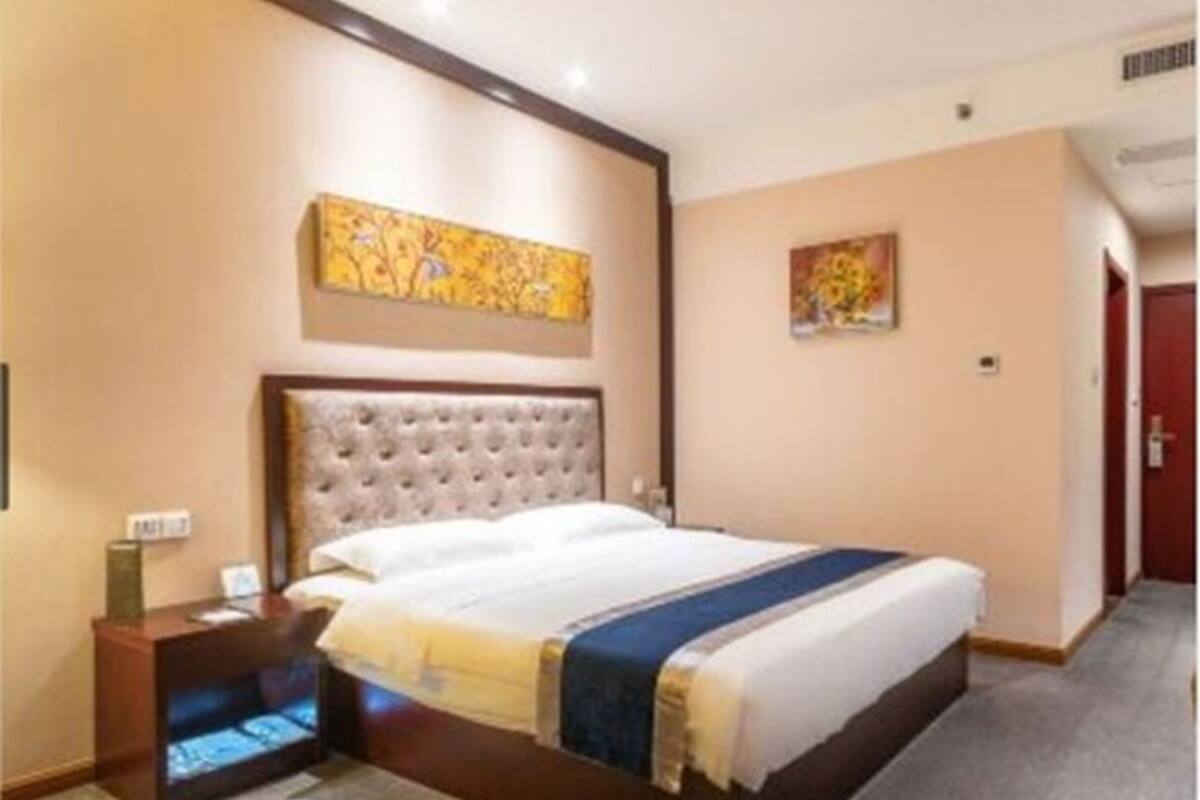Ein Hotelzimmer mit einem großen Bett, einem Nachttisch, einem Wandbild und einer Tür im Hintergrund.