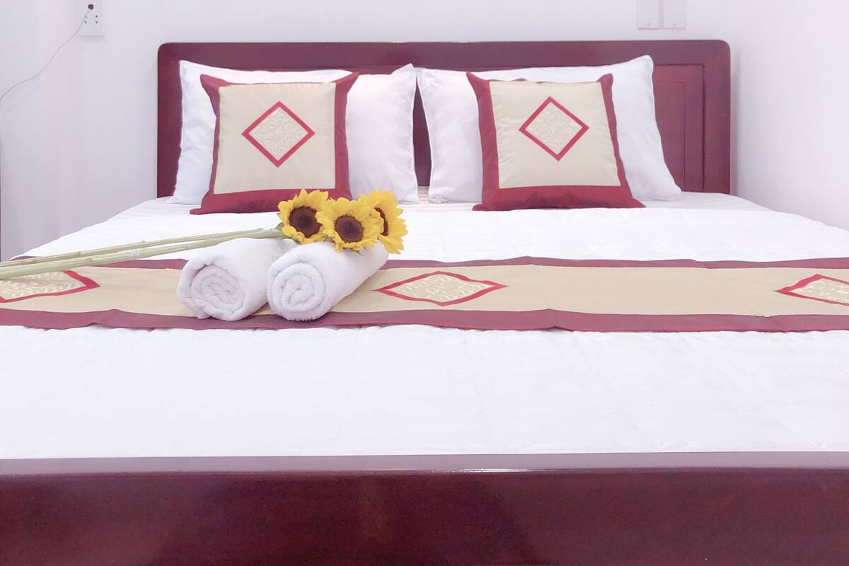 A neatly made bed with white and red bedding, a decorative wall light, and a bouquet of sunflowers.