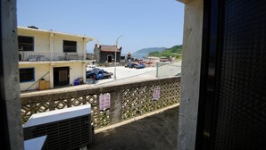 Un balcon donnant sur un immeuble avec un toit en tuiles, des voitures garées et un ciel dégagé.