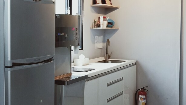 Une cuisine équipée d’un réfrigérateur en acier inoxydable, d’un évier, d’un plan de travail, d’un extincteur et de luminaires suspendus.