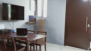 Une pièce avec une table en bois, des chaises, un ordinateur portable, un téléviseur à écran plat et une porte.