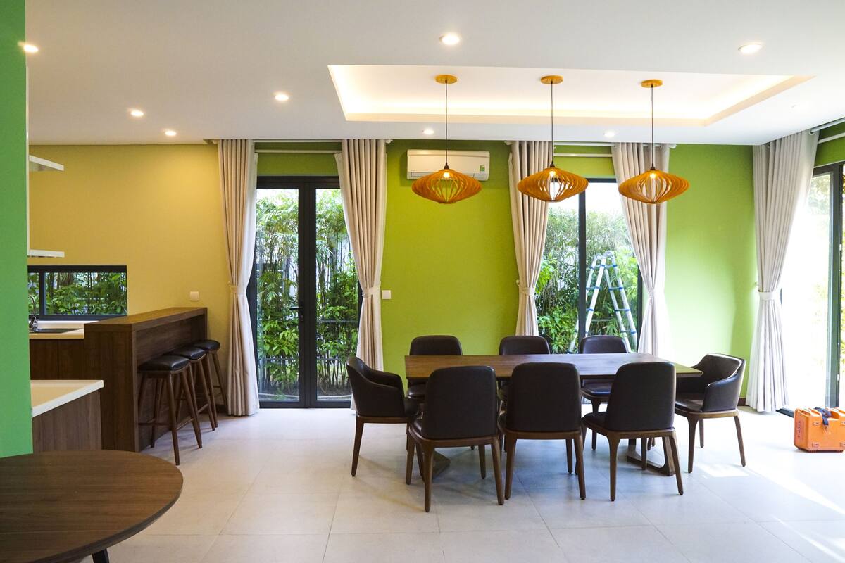 A dining area with a table and chairs, a bar with stools, and large windows with curtains.