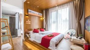 A modern bedroom with a wooden ceiling, a large bed with red and white bedding, a bedside table with a fan, and a view of the city through large windows.