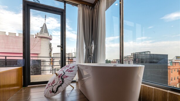 A modern bathroom with a large bathtub, a wooden bench, and a view of a cityscape through large windows.