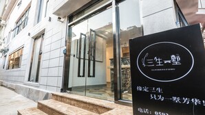 A building entrance with a glass door, a black sign with white text, and a set of stone steps leading up to the door.