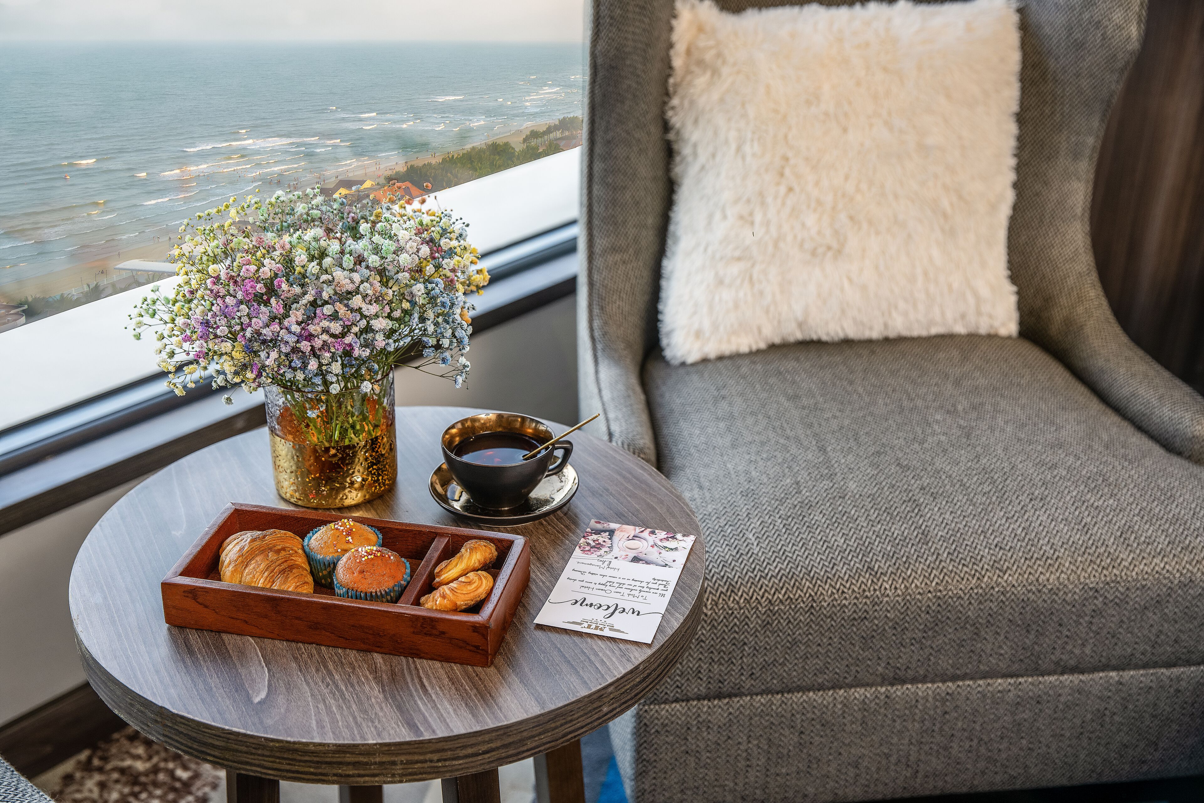 Een ronde tafel met een schaal gebak, een bloevas, een kop koffie en een menukaart.