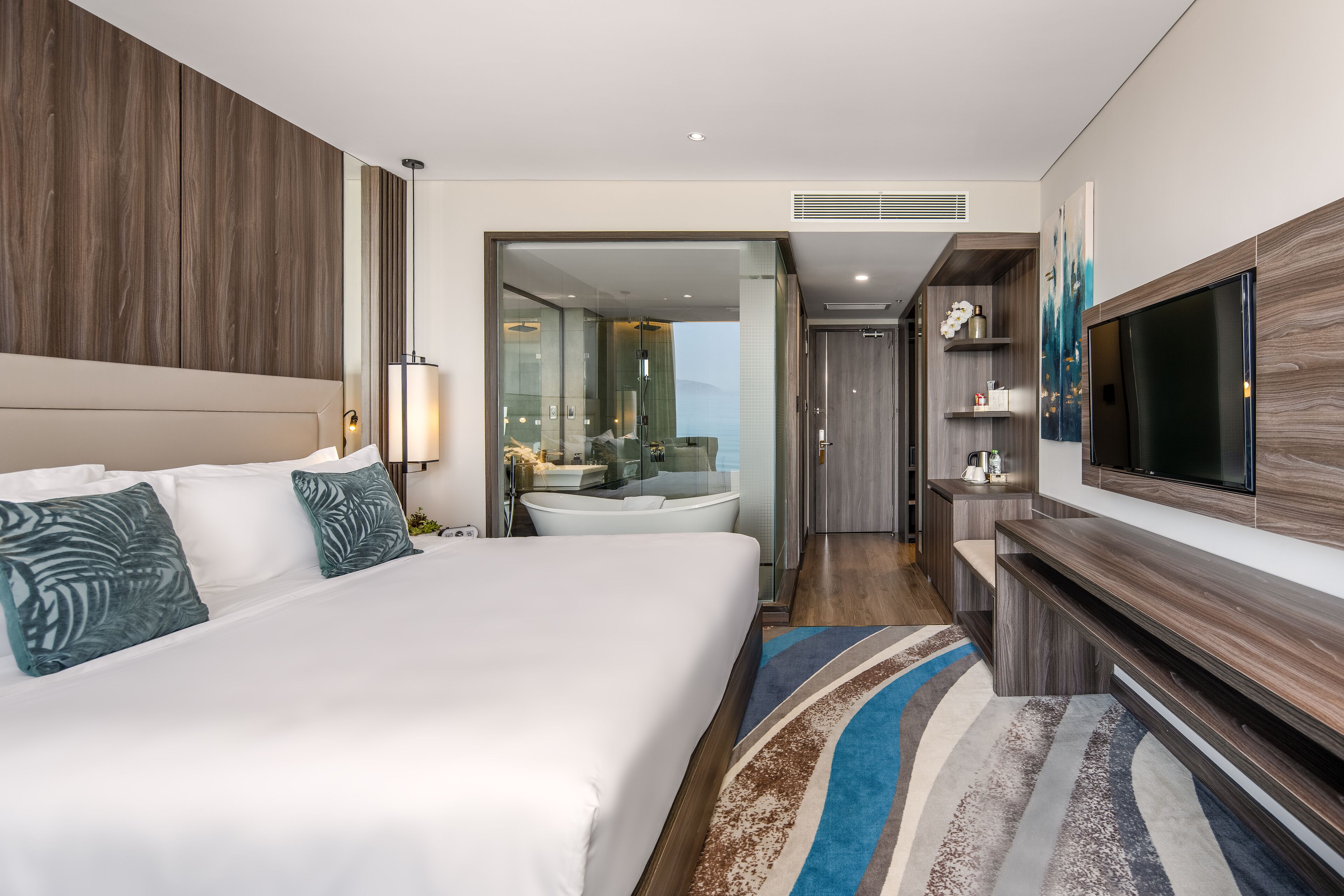 Ein modernes Hotelzimmer mit einem großen Bett, einem Fernseher, einem Badezimmer mit Badewanne und Meerblick.