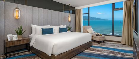 A modern hotel room with a large bed, a seating area, and a view of the sea.