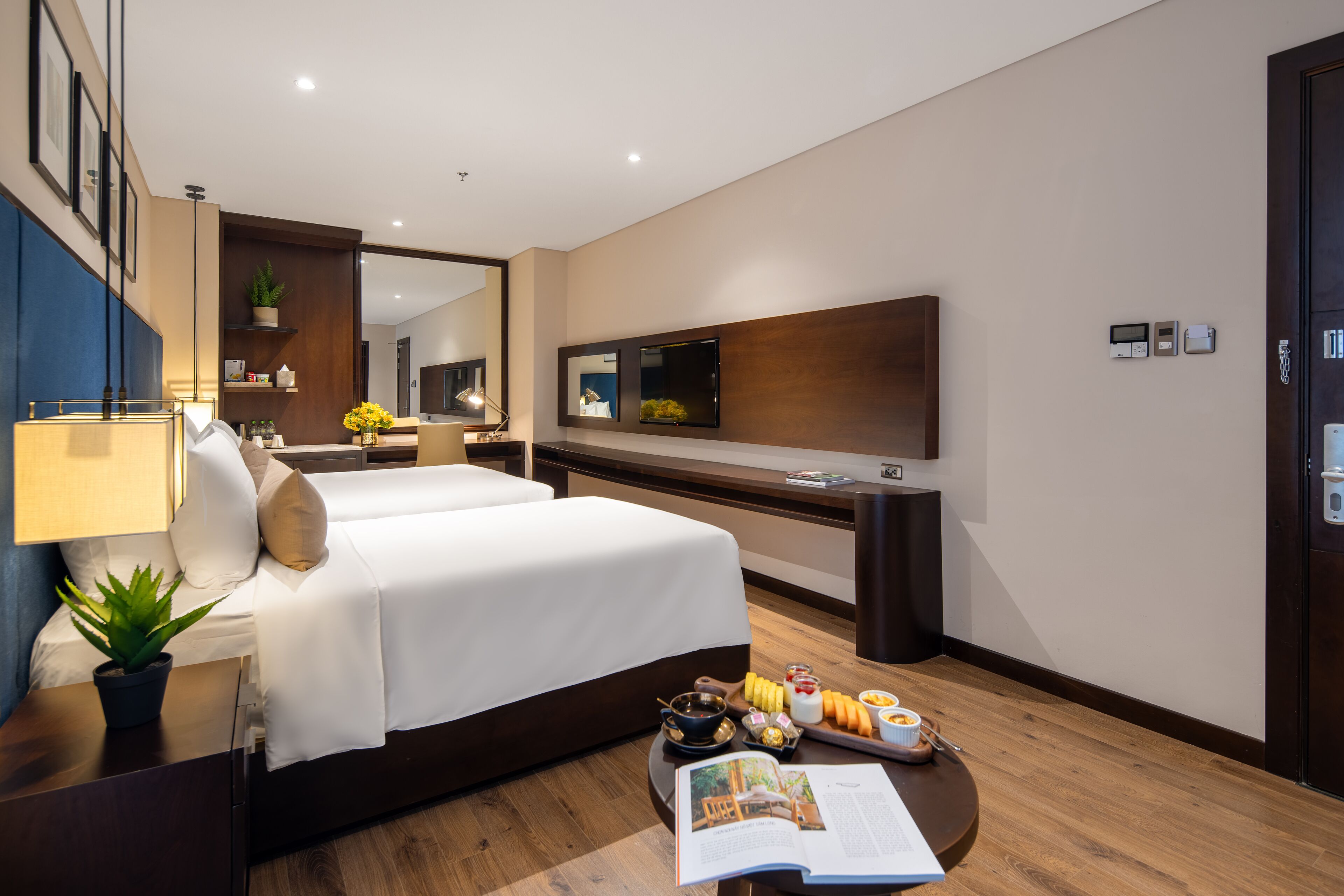 A modern hotel room with a large bed, a desk with a computer, a flat-screen TV, and a dining area with a tray of food.