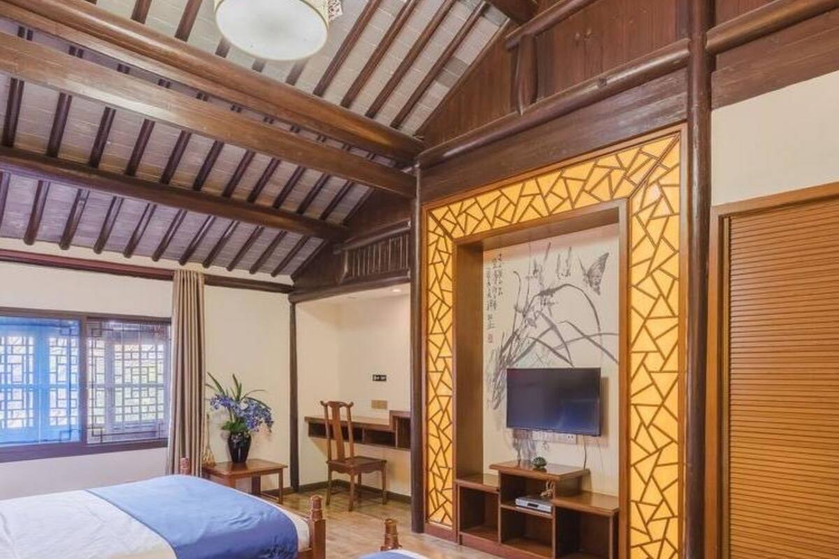 A hotel room with two beds, a desk, a chair, a TV, and a decorative screen.