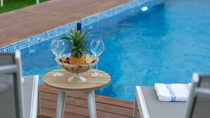 A poolside table with a fruit bowl and two wine glasses, surrounded by lounge chairs. - Dov Garden apartment with private pool (Tiberias)