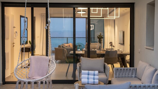 A modern outdoor seating area with a hanging chair, cushioned sofas, and a dining table. - Dov Garden apartment with private pool (Tiberias)