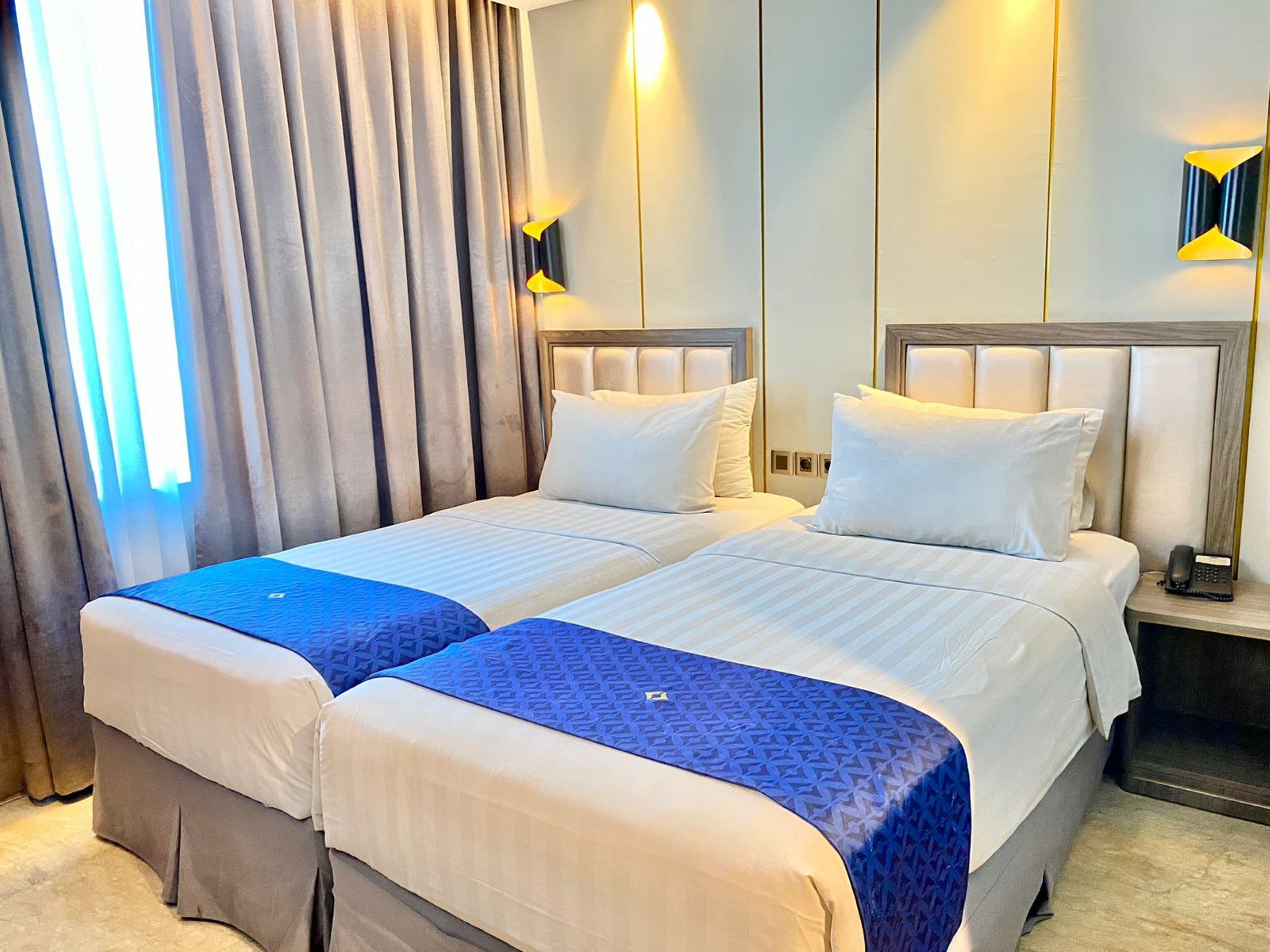 Une chambre d’hôtel avec deux lits, chacun doté d’une tête de lit et d’oreillers, une table de chevet avec un téléphone et une fenêtre avec des rideaux.